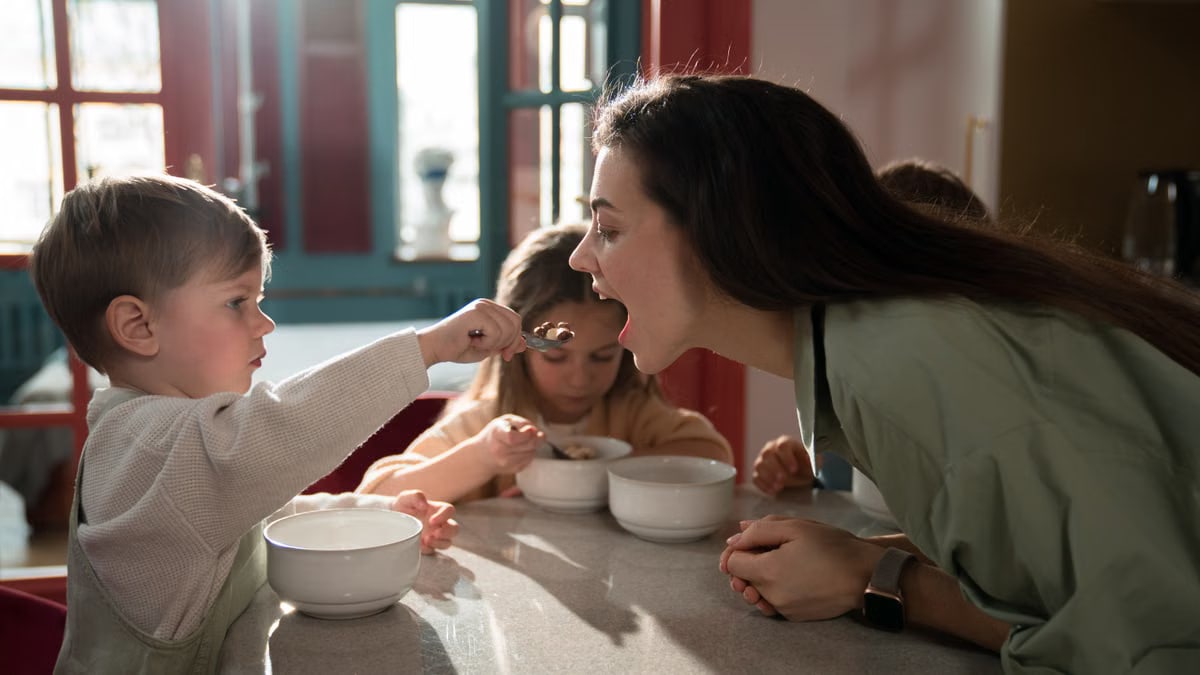 A mother enjoys a playful breakfast moment with her children, sharing quality family time indoors.